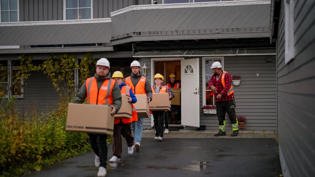 Scene fra reklamefilm for PEAB. Bildet viser PEAB-ansatte som bærer flyttekasser mens bas overser arbeidet.