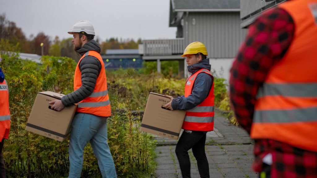 Scene fra reklamefilm for PEAB. Bildet viser PEAB-ansatte som bærer flyttekasser mens bas overser arbeidet.