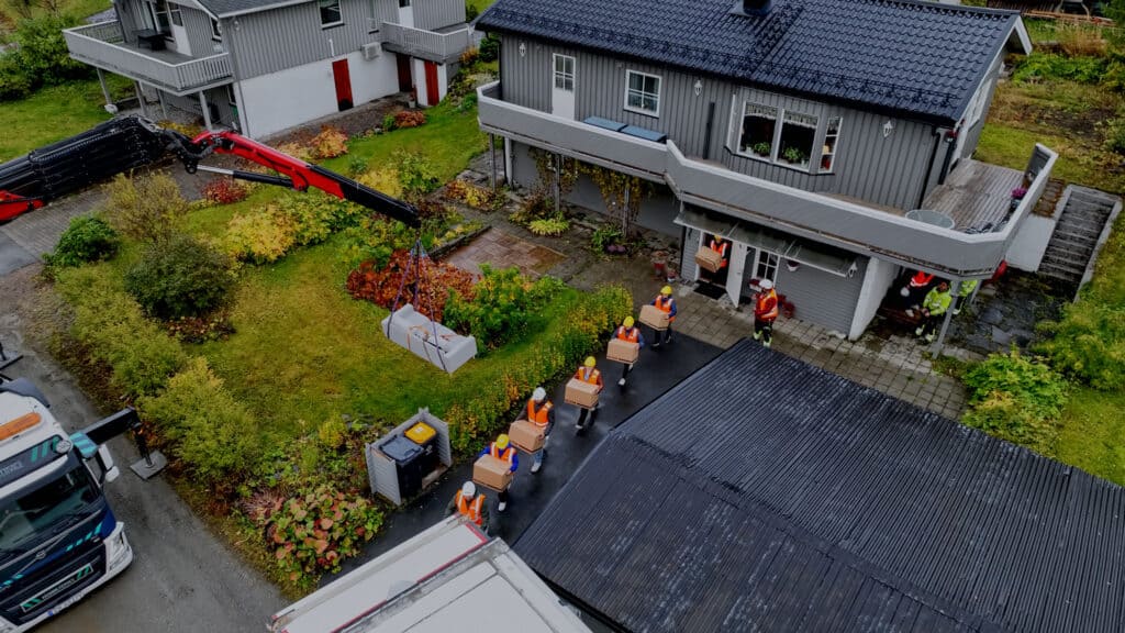 Scene fra reklamefilm for PEAB. Bildet er et oversiktsbilde tatt med drone som viser PEAB-ansatte på rekke som bærer ut flyttekasser fra huset.