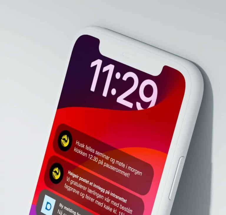 En smarttelefon viser klokken 11:29 på skjermen, med varsler på norsk mot en rød og oransje bakgrunn med grader. Telefonen er litt vinklet og plassert mot en lys overflate.