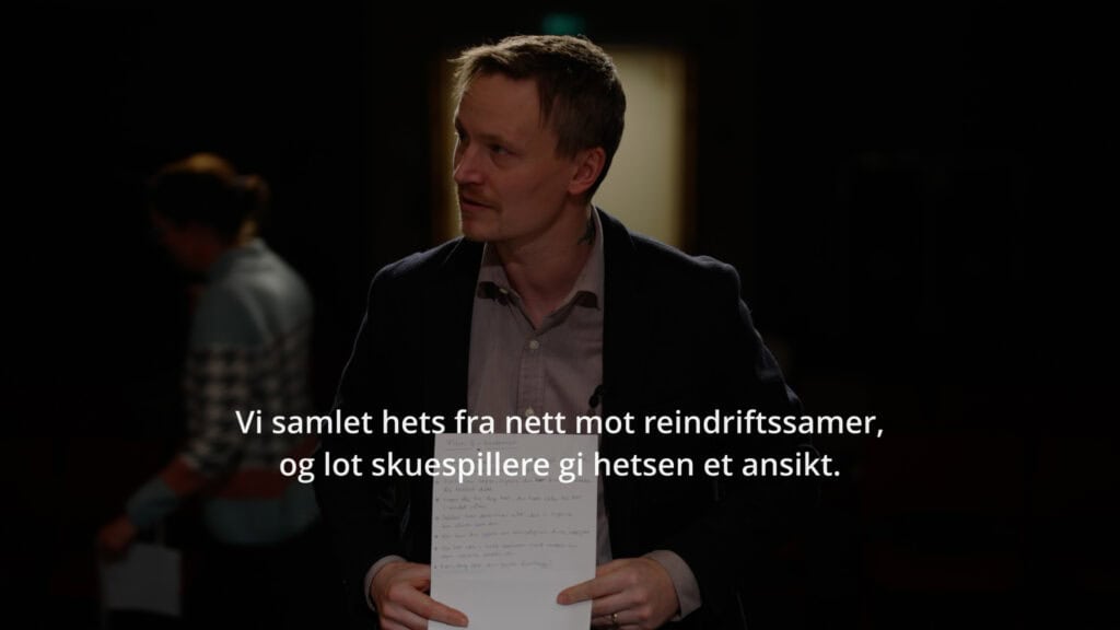 Scene fra reklamefilm i holdningskampanje mot hets og hatytringer på nett rettet mot reindriftsutøvere og samer. En mann i dress holder et ark, stående i et svakt opplyst rom med uskarpe skikkelser i bakgrunnen. Tekst sier: Vi samlet hets fra nett mot reindriftssamer og lot skuespillere gi hetsen et ansikt.