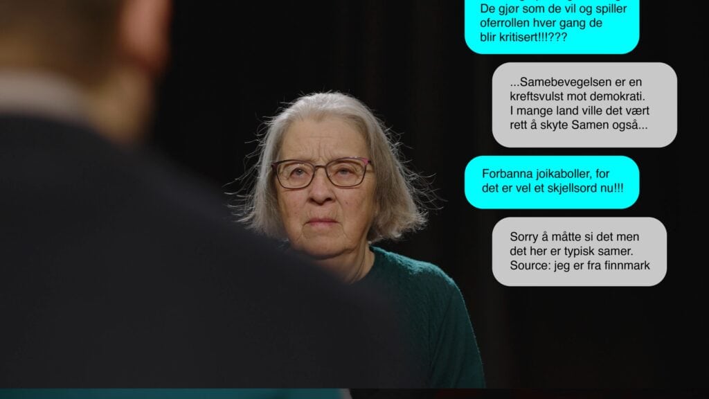 En eldre kvinne med briller og grått hår iført en grønn genser ser tankefull ut mens hun lytter til noen utenfor kameraet. På skjermen vises chatbobler med utdrag fra virkelige meldinger fra nettet.