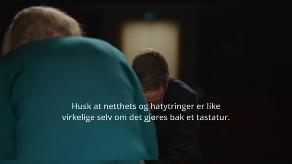 To uskarpe personer er bøyd fremover, ansikter for det meste skjult. Norsk tekst over bildet lyder: Husk at netthets og hatytringer er like virkelige selv om det gjøres bak et tastatur. Skjermbilde fra holdningskampanjen for Reinfakta.