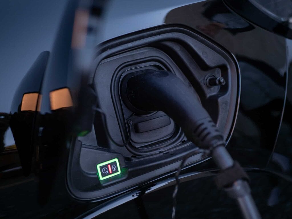 Nærbilde av en elbil som lades, som viser ladekabelen koblet til kjøretøyets port, med et grønt opplyst display som indikerer ladestatusen.