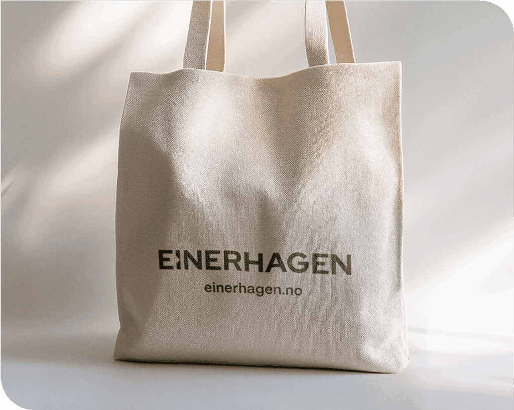 En beige bæreveske med teksten EINERHAGEN og einerhagen.no trykt i svart på forsiden, stående oppreist på en hvit flate med dempet belysning.